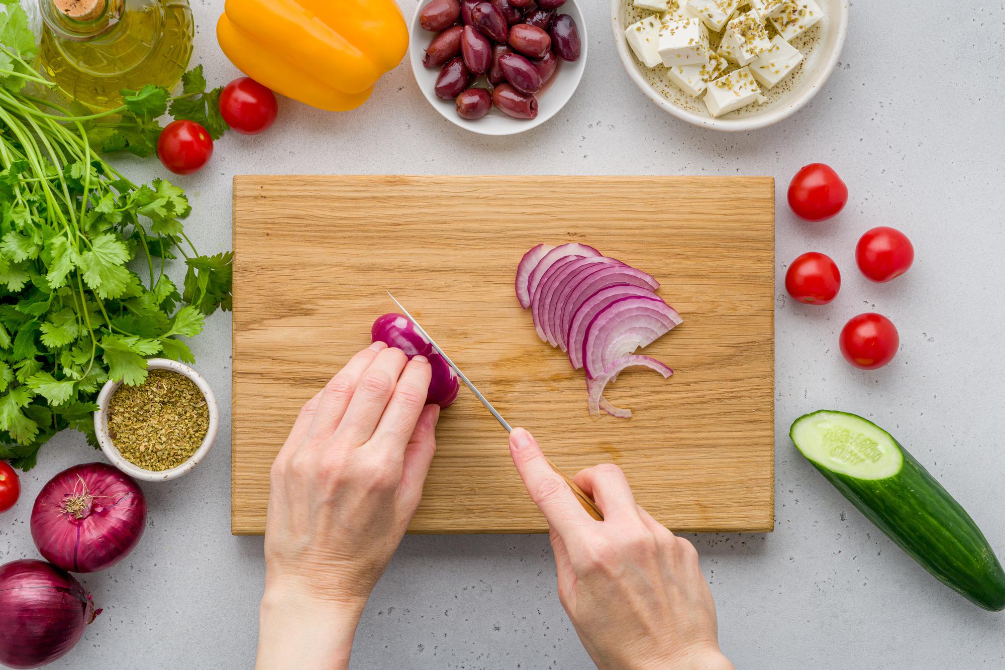 Hands preparing vegetables on wooden board with neat mise en place