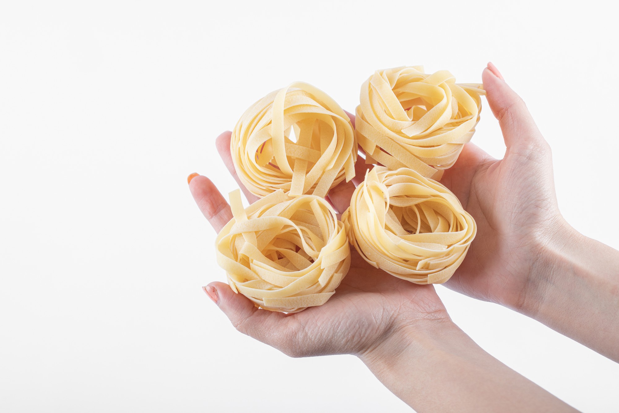 Hands pulling fresh pasta strands in a bright kitchen
